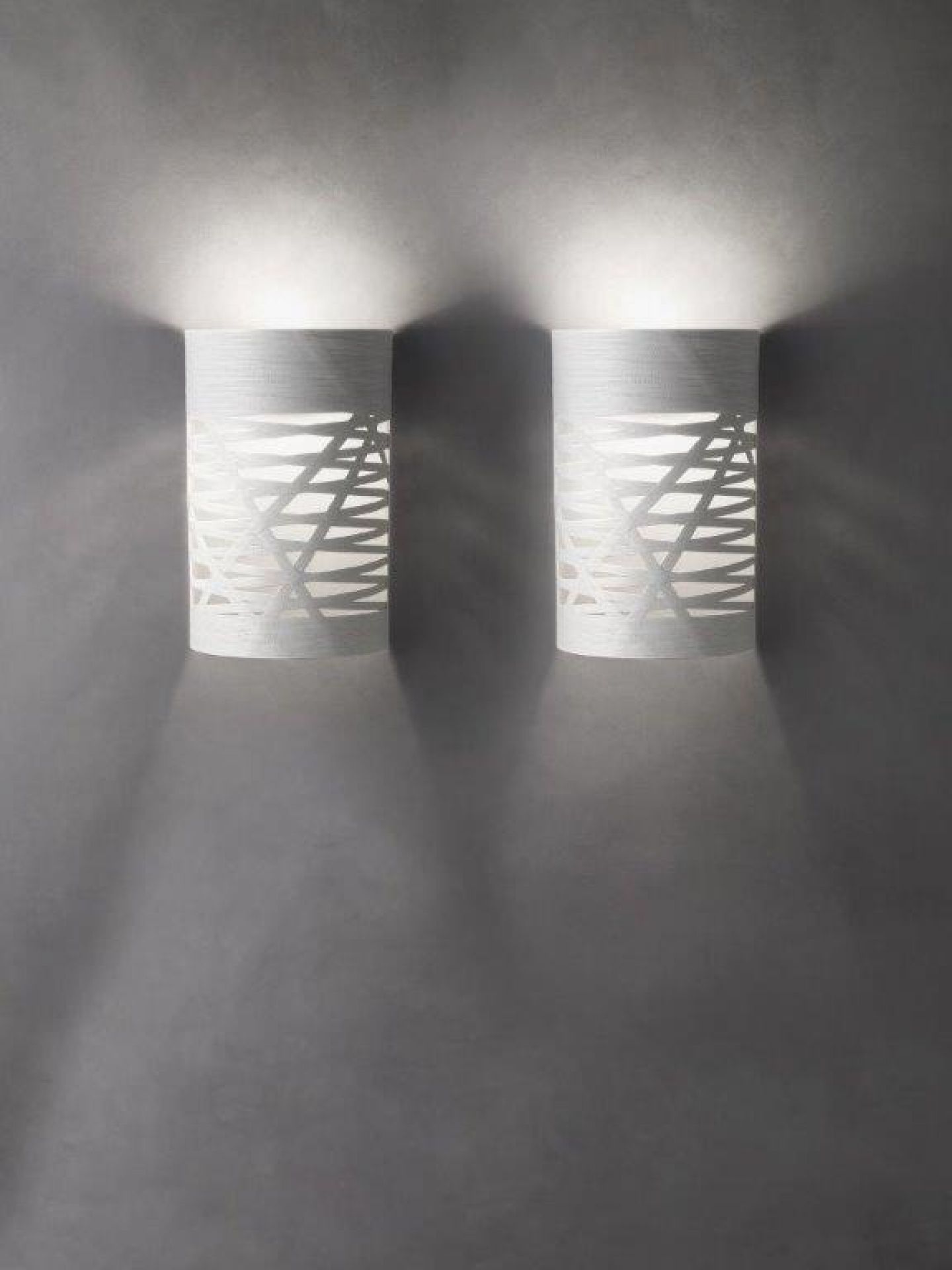 Zwei moderne Tress Wandleuchten von Foscarini in Weiß mit geometrischem Muster an einer grauen Wand.