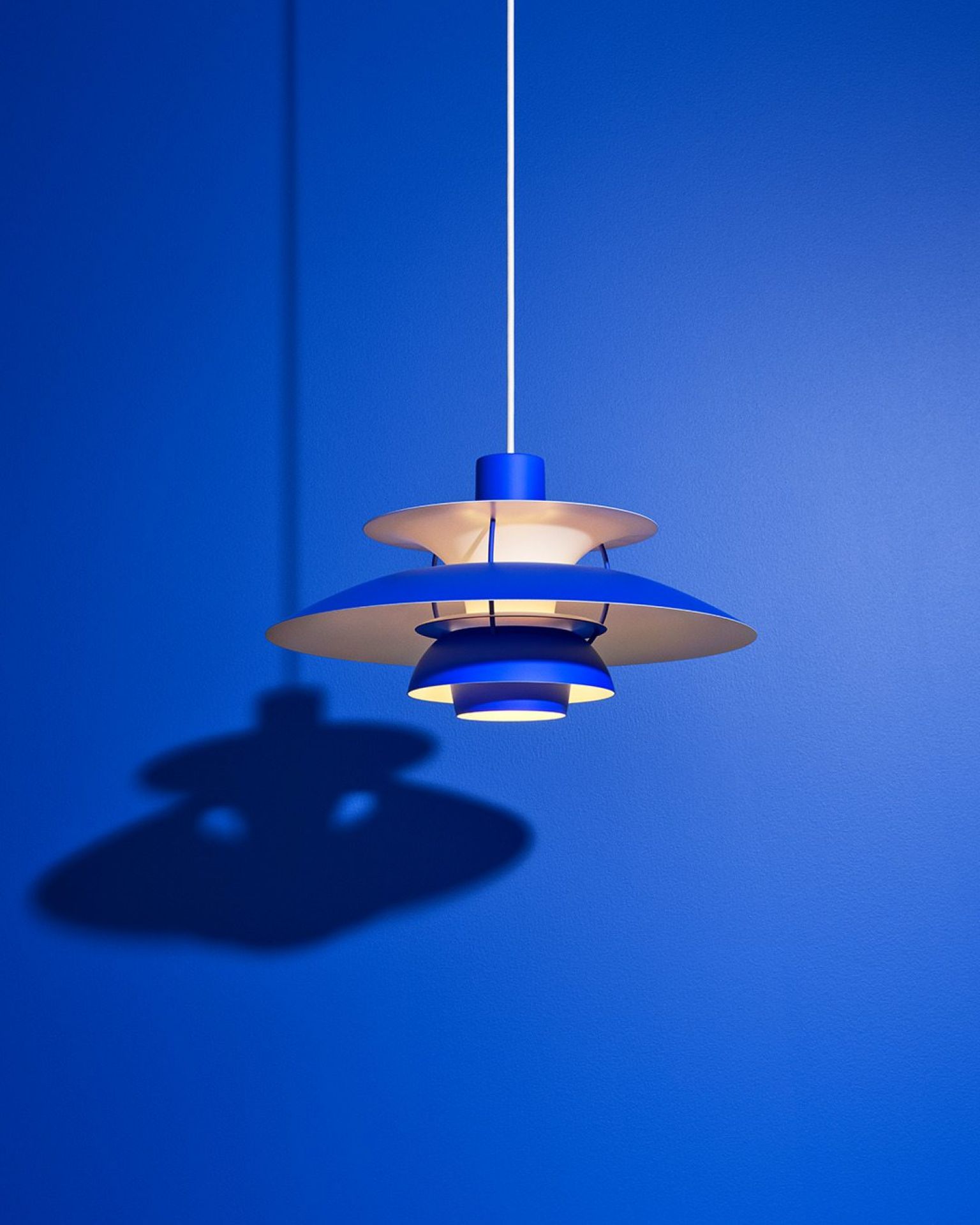 Blaue PH 5 Mini Pendelleuchte von Louis Poulsen vor blauem Hintergrund mit Schatten.