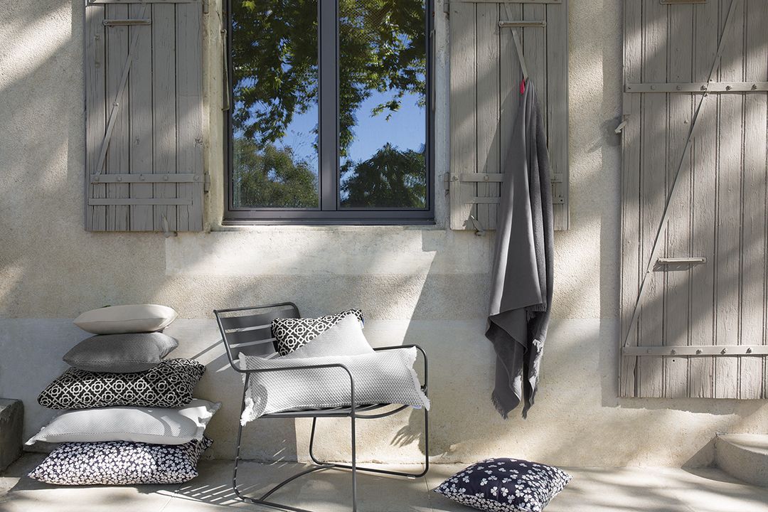 Surprising Fermob Sessel für den Garten mit Kissen und Decke vor rustikalem Hintergrund.