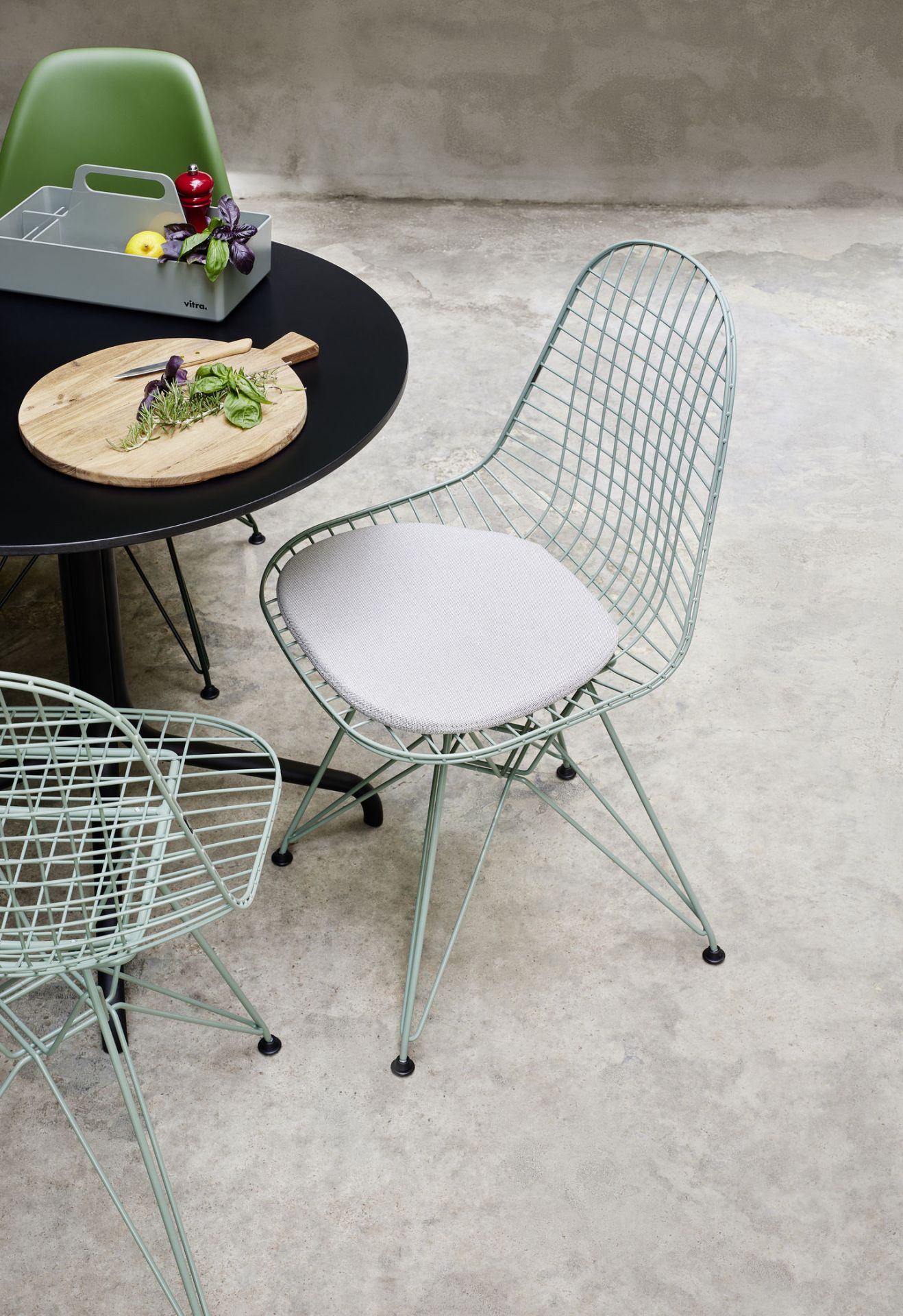 Nahaufnahme eines mintgrünen Vitra DKR Wire Chair Stuhls mit grauem Sitzkissen an einem Esstisch.