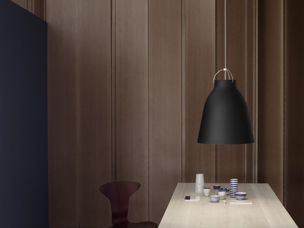 Schwarze Caravaggio Pendelleuchte von Fritz Hansen über einem Esstisch mit Geschirr und Holzstuhl.
