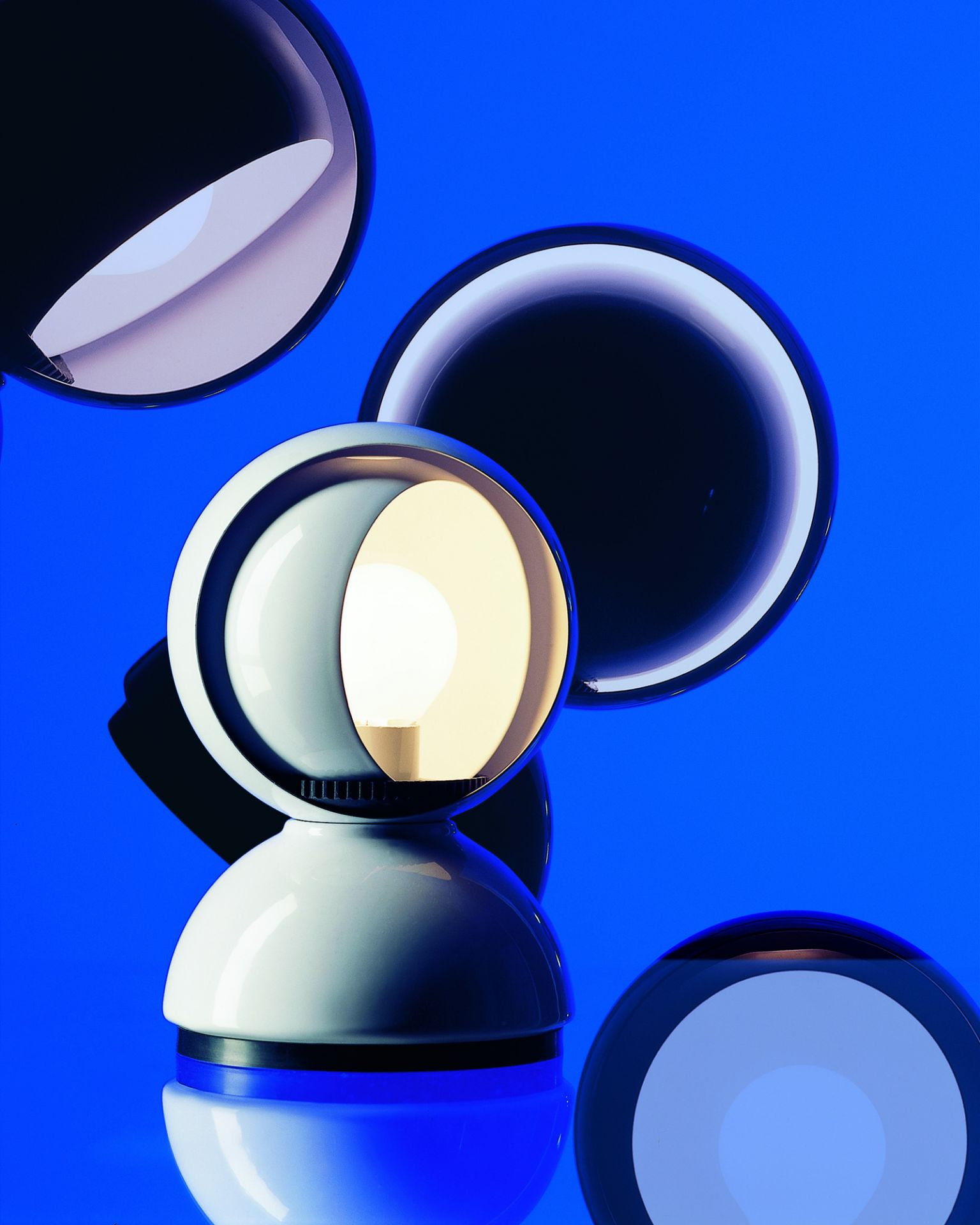 Weiße Artemide Eclisse Tischleuchte mit verstellbarem Schirm und warmem Licht auf blauem Hintergrund.