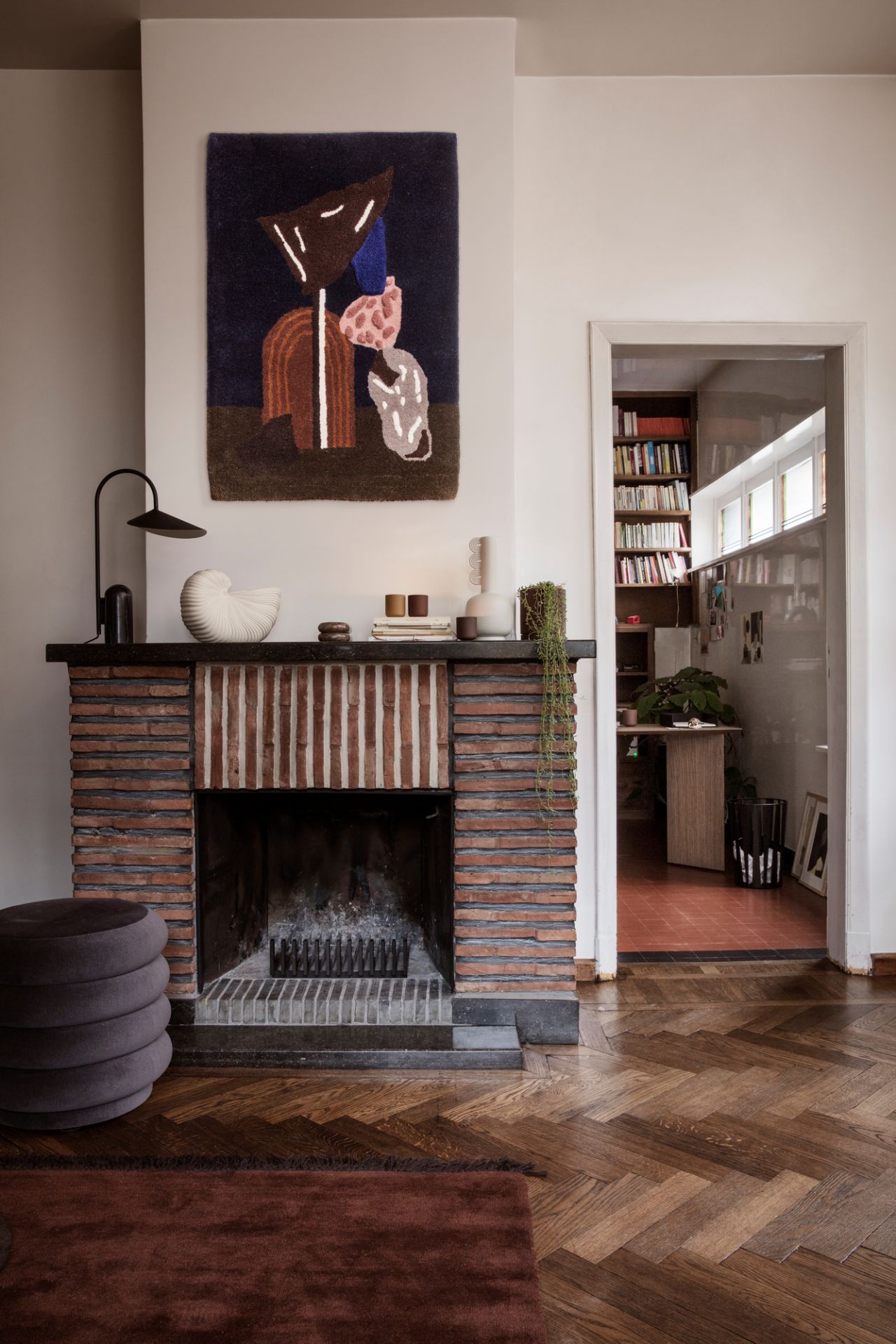 Dekoratives Wohnzimmer mit Kamin, Shell Pot Vase von Ferm Living und abstrakten Wandteppich für stilvolles Interieur.