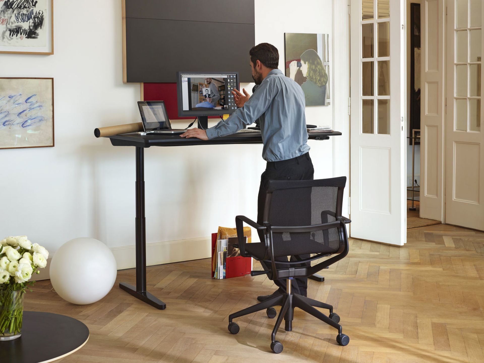 Schwarzer Physix Studio Bürodrehstuhl von Vitra vor einem höhenverstellbaren Schreibtisch mit Person. Ergonomischer Bürostuhl mit Rollen.