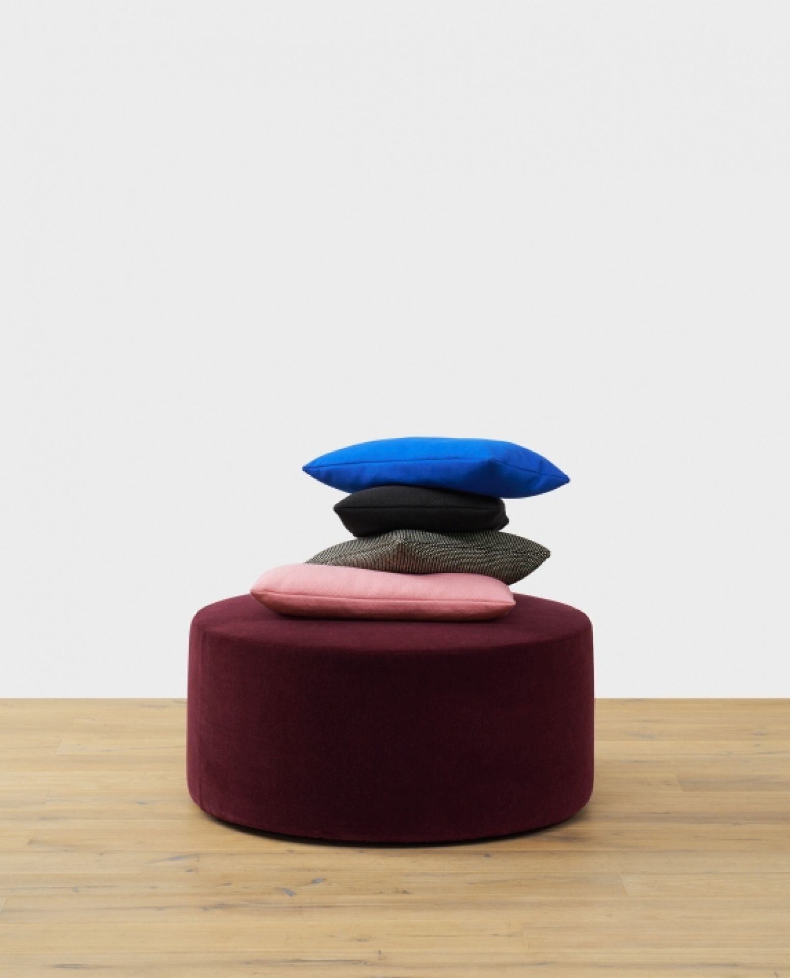 SF06 Kerman Modulsofa e15: Burgunderfarbener Hocker mit gestapelten Kissen in Blau, Schwarz und Rosa.