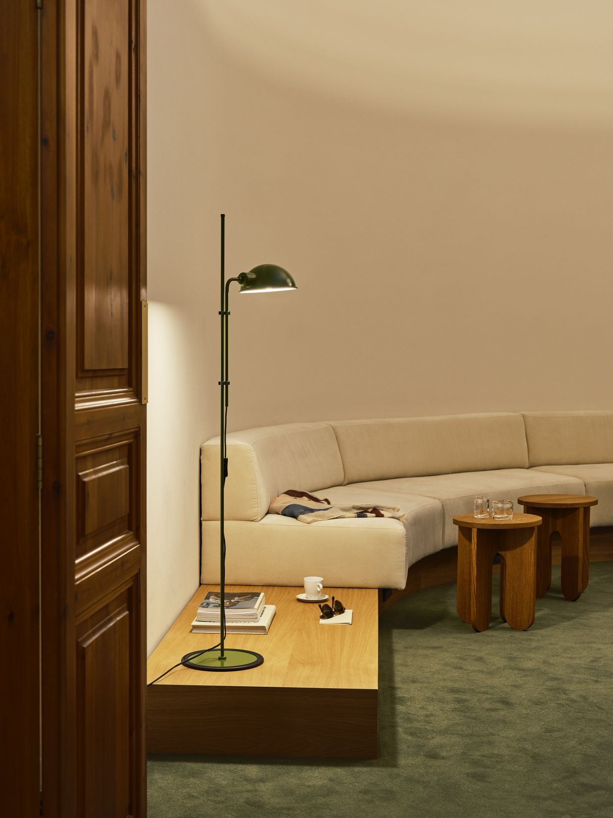 Moosgrüne Funiculí Stehleuchte von Marset im Wohnzimmer mit Sofa und Holztischen.