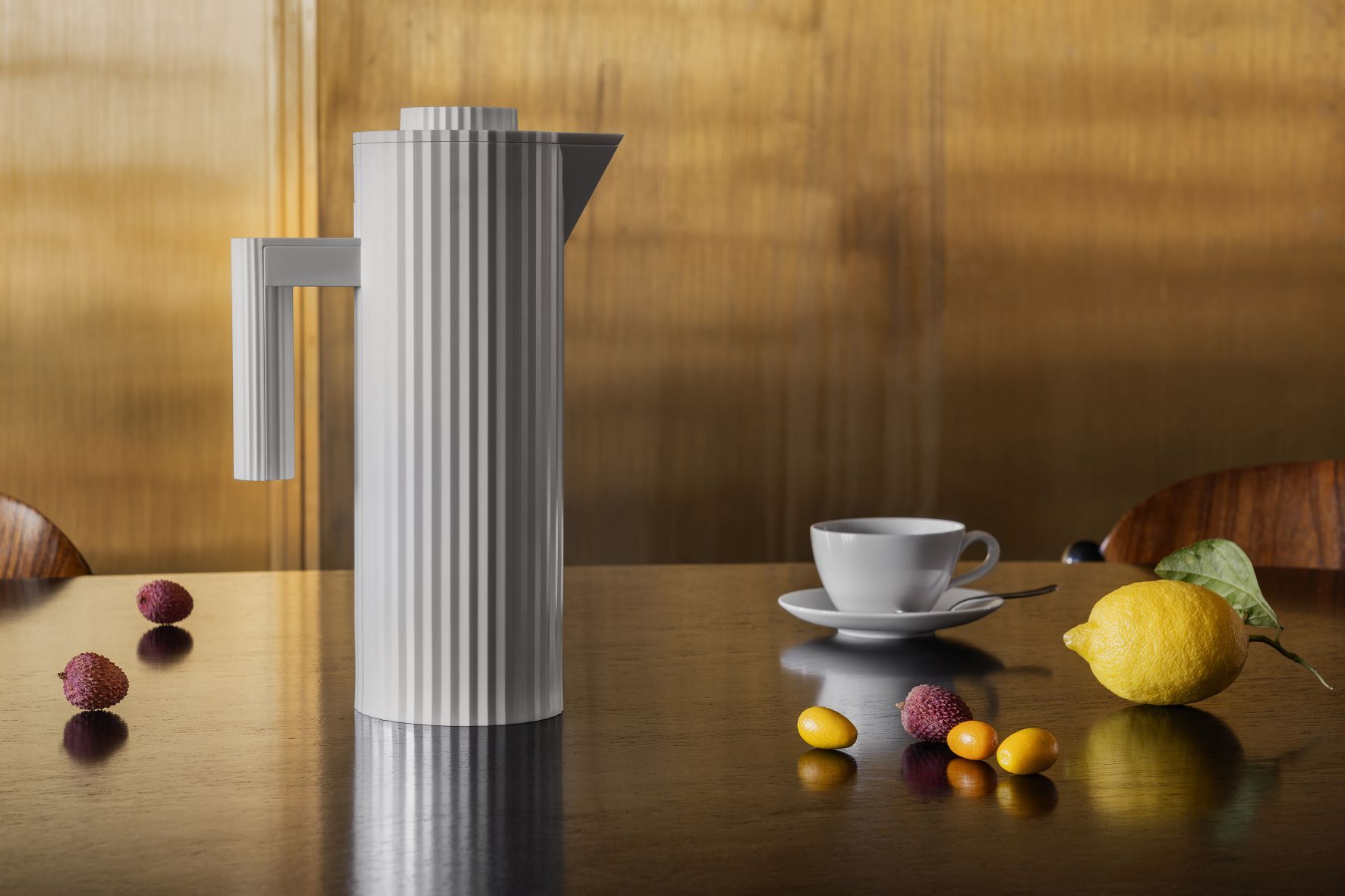 Weiße Alessi Plissé Isolierkanne MDL12 auf Tisch mit Tasse, Zitrone und Kumquats.