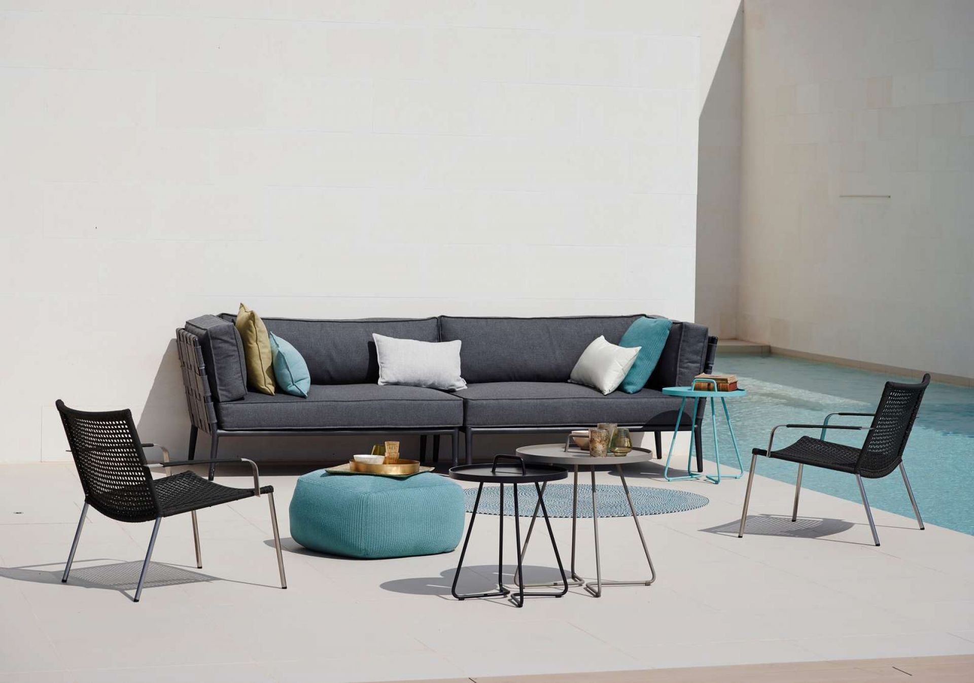 Conic Outdoor Sofa von Cane-Line, graues 2-Sitzer Modulsofa rechts mit Outdoor-Möbeln und Pool.