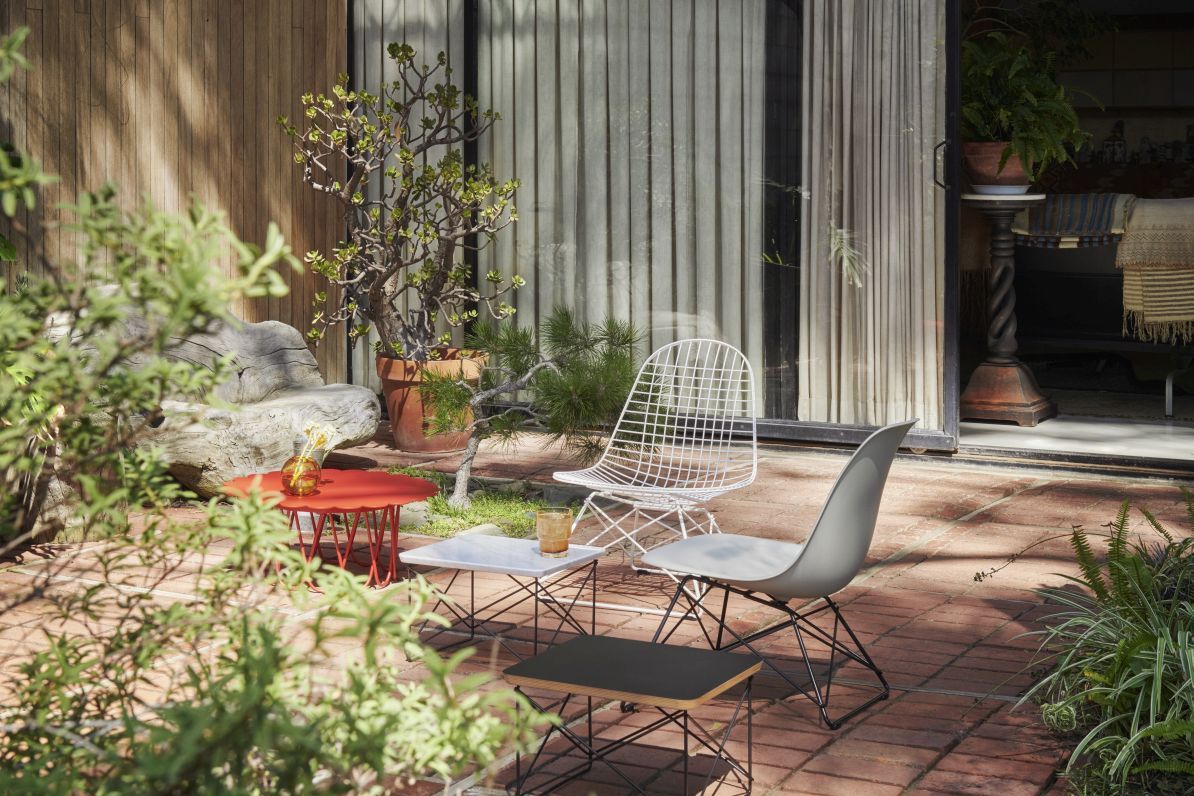 Eames Stuhl von Vitra, graue Sitzschale mit schwarzem Metallgestell, im Garten auf Backsteinterrasse.