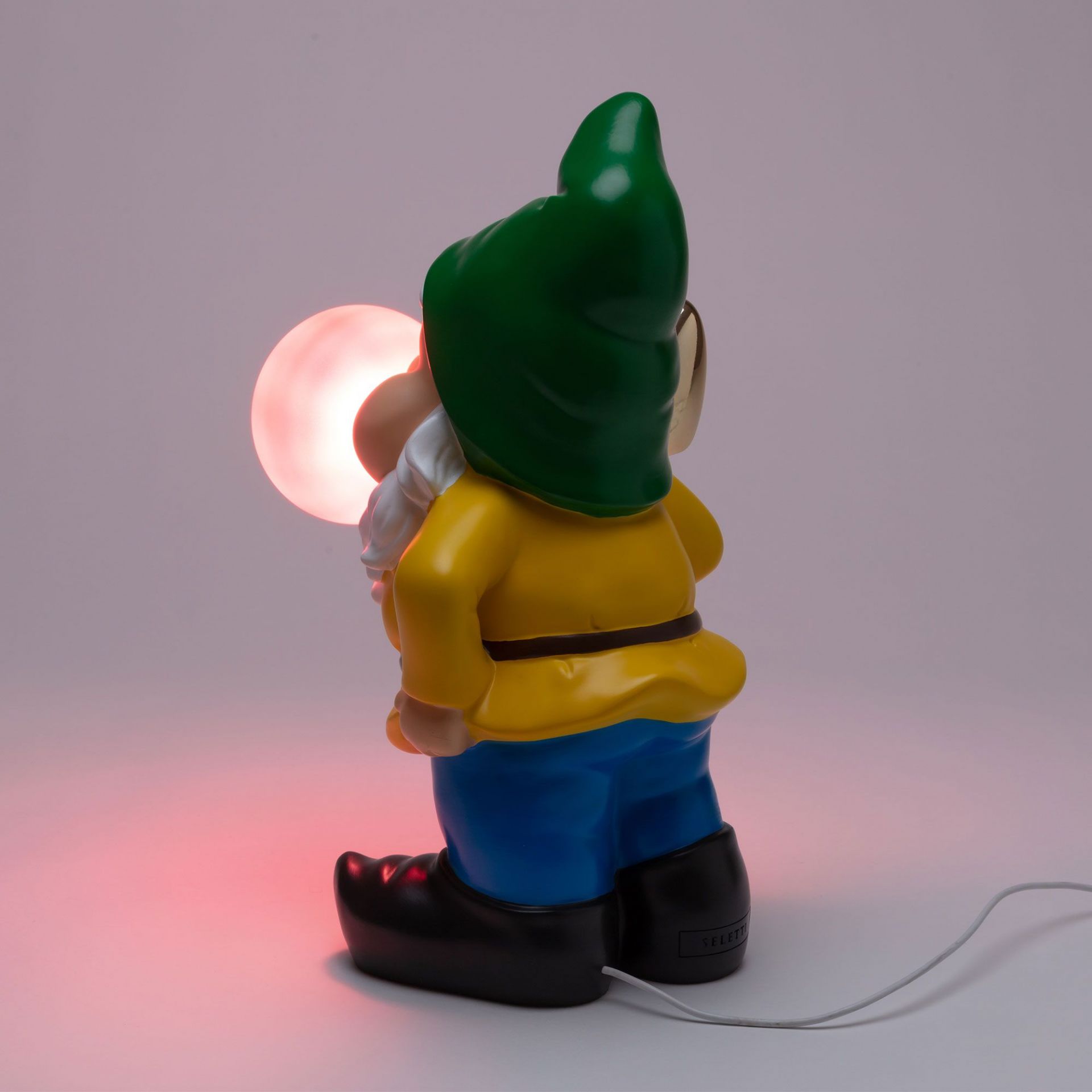 Seletti Gummy Working Leuchte: Rückansicht der Zwergenlampe mit gelber Jacke, blauer Hose und leuchtender Kugel.