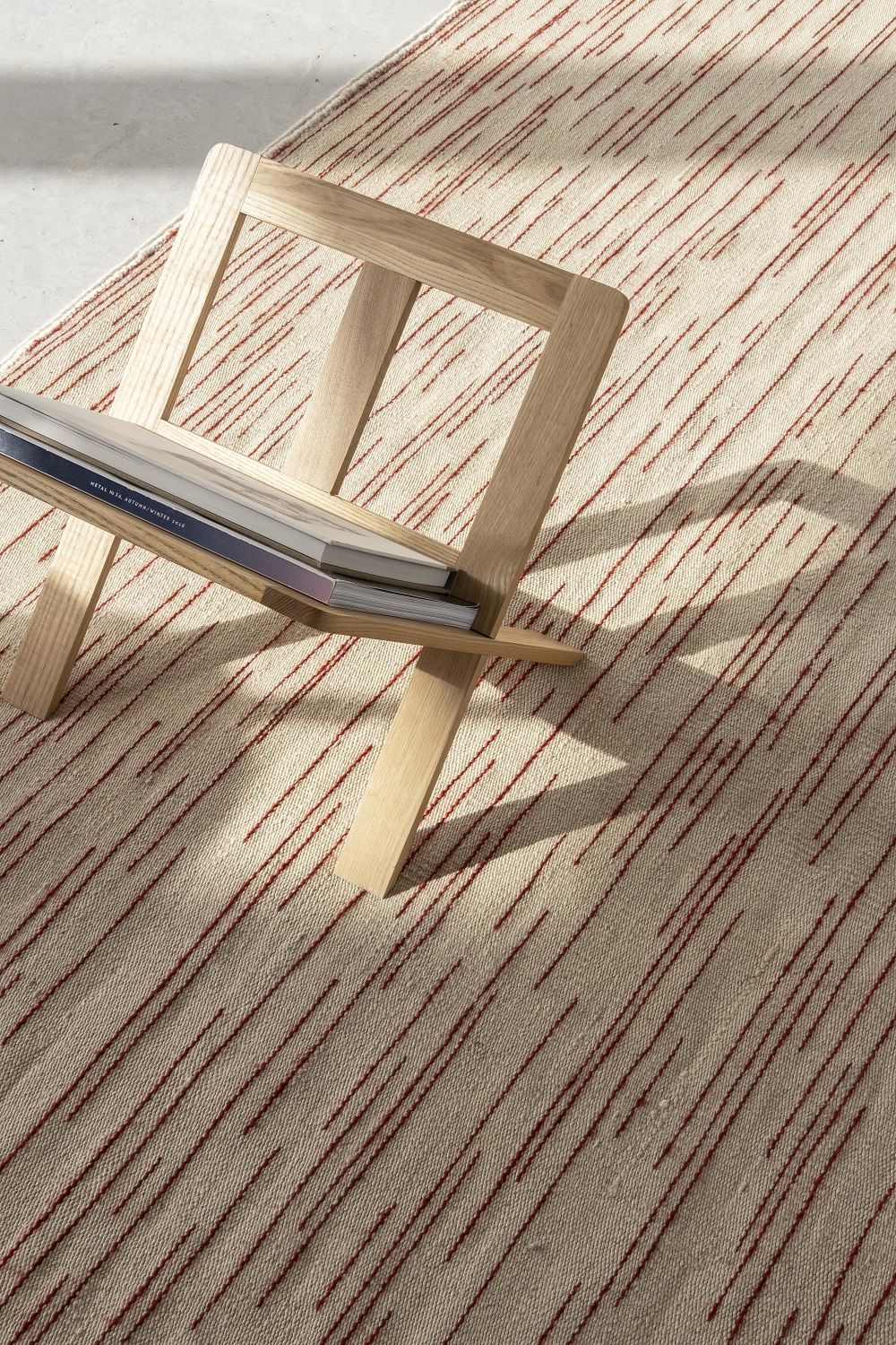 Detailaufnahme des Nanimarquina Teppichs Doblecara Rug mit rotem Streifenmuster und Holzstuhl.