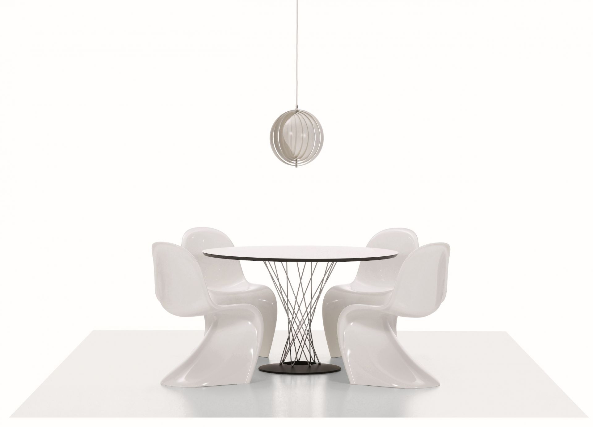 Vier weiße Panton Stühle um einen runden Tisch mit Drahtgestell und Lampe.