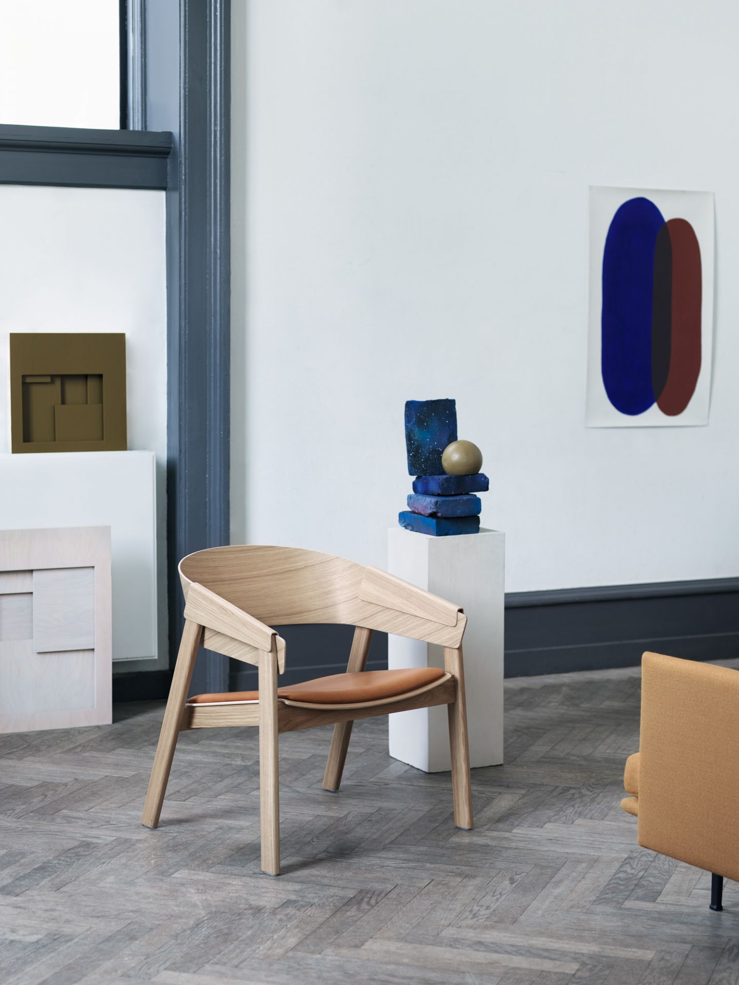 Muuto Cover Lounge Chair Stuhl aus hellem Holz mit braunem Ledersitz in modernem Ambiente.