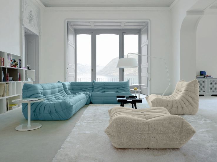 Helles Wohnzimmer mit türkisfarbenem Togo Eckteil Sofa von ligne roset und passenden Sesseln auf einem weißen Teppich.