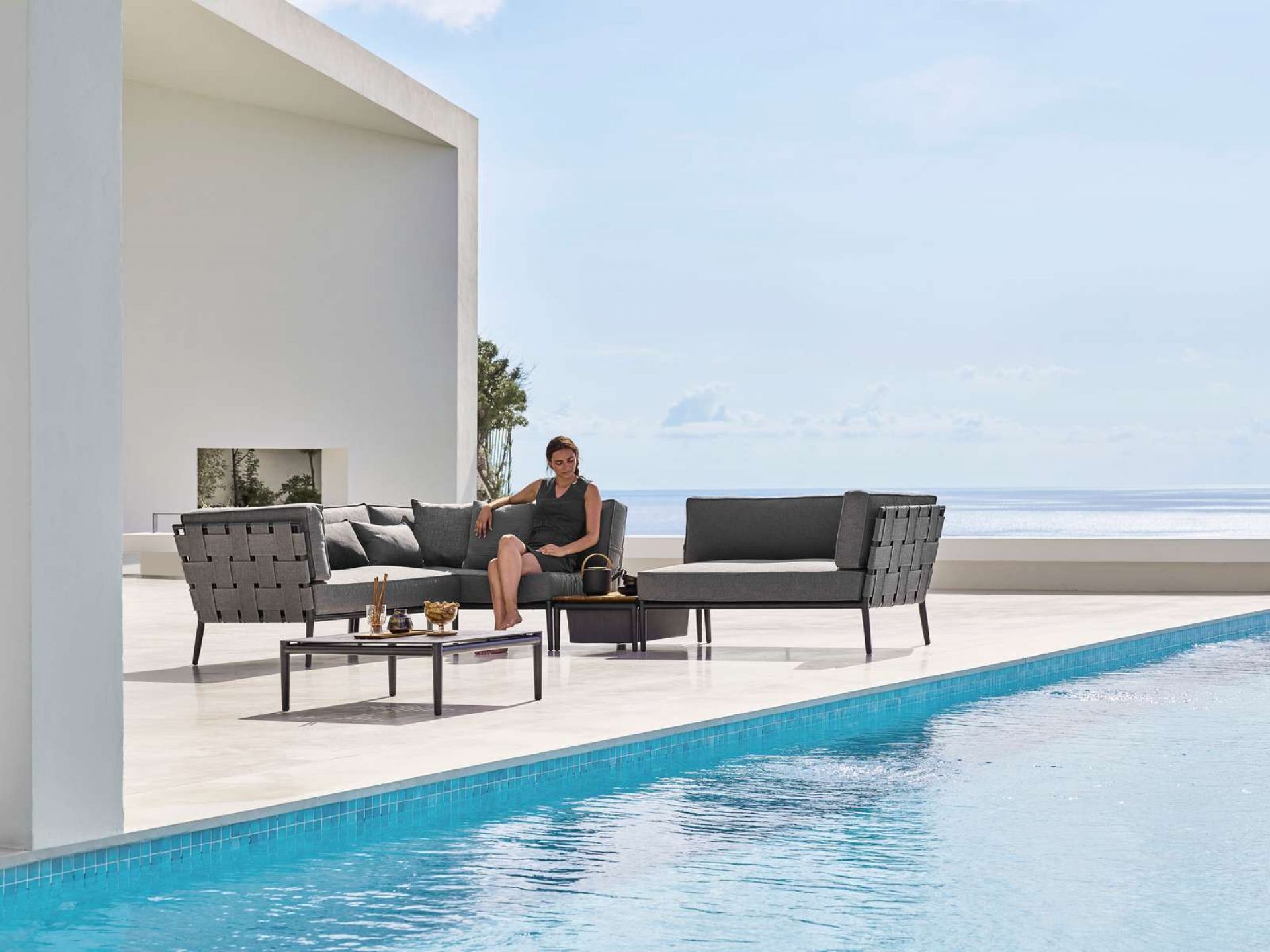 Frau entspannt auf Cane-Line Conic Outdoor Modulsofa rechts, graues Lounge-Set am Pool.