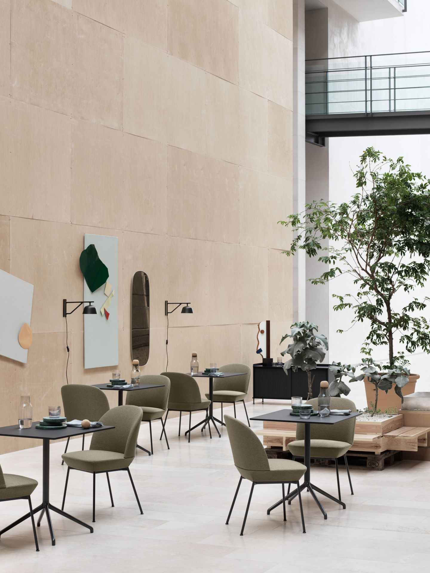 Innenaufnahme mit mehreren Still Cafe Table Beistelltischen von Muuto und grünen Stühlen in einem hellen Raum.