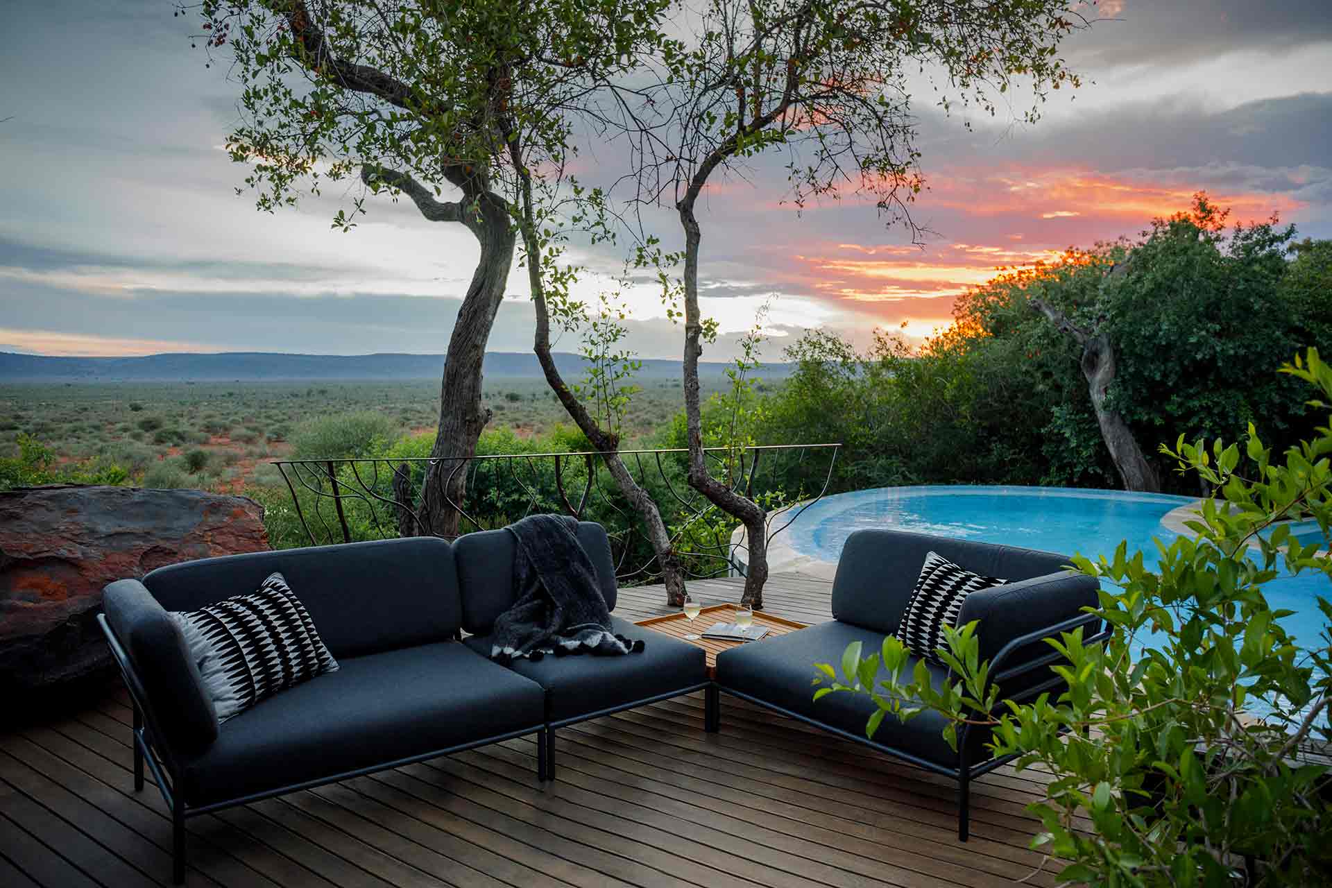 Houe Level Outdoor Sofa Ecke links auf Holzterrasse mit Pool und afrikanischer Landschaft.
