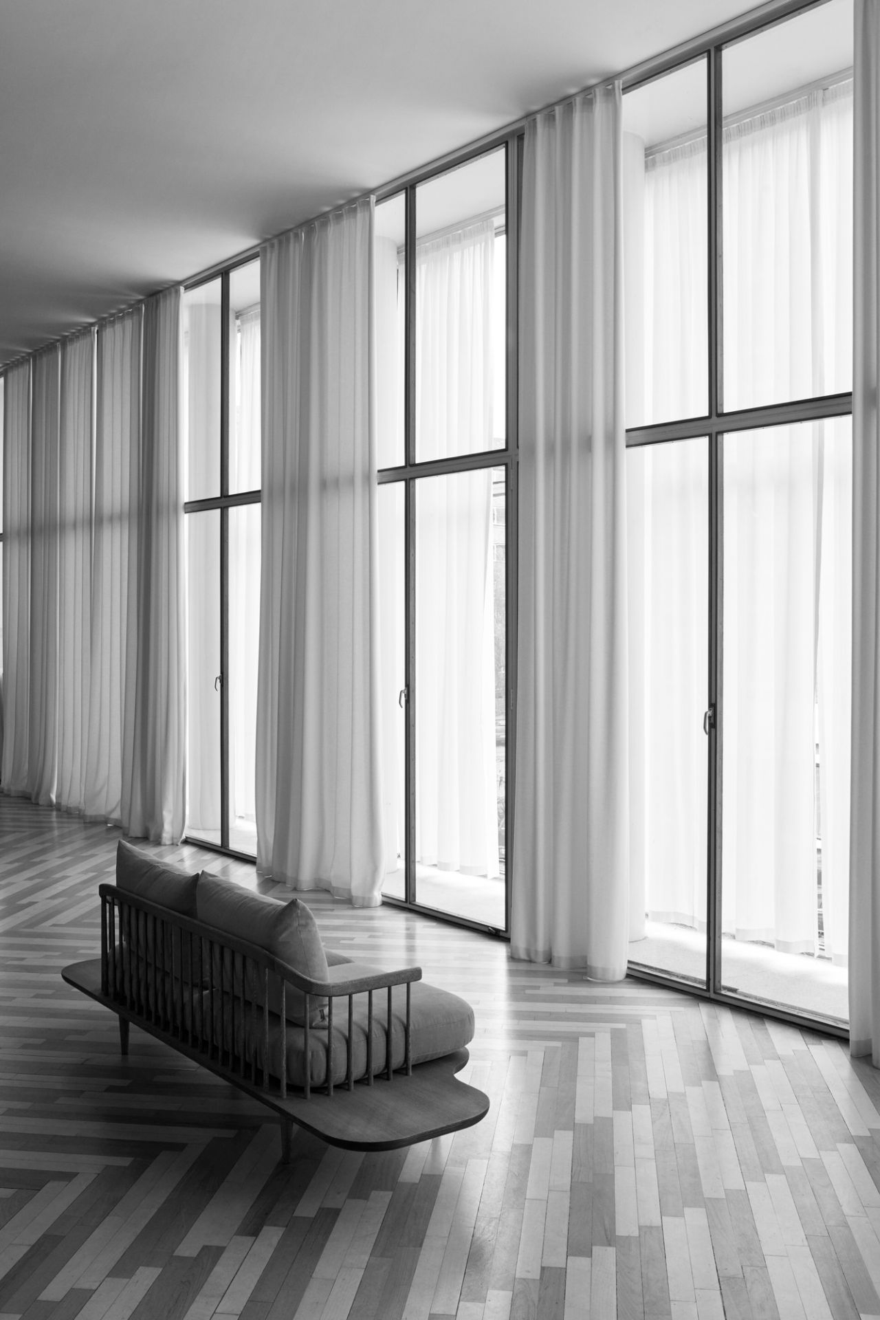 Schwarz-weißes Foto des Fly Lounge 2-Sitzer Sofas von AndTradition mit Eichengestell und grauer Polsterung vor Fensterfront.