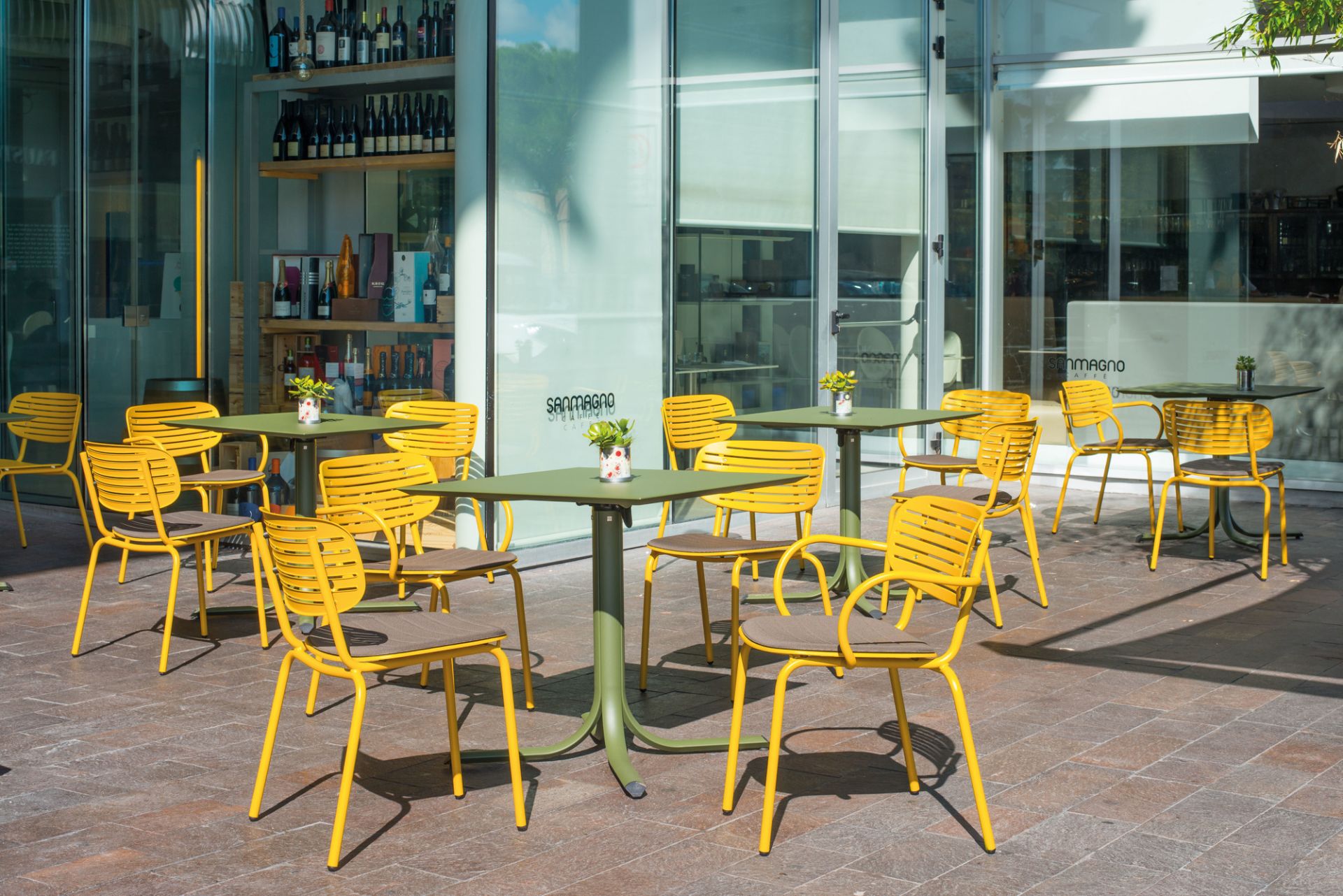 Gelbe Mom Stühle von Emu mit olivgrünen Tischen im Außenbereich eines Cafés.