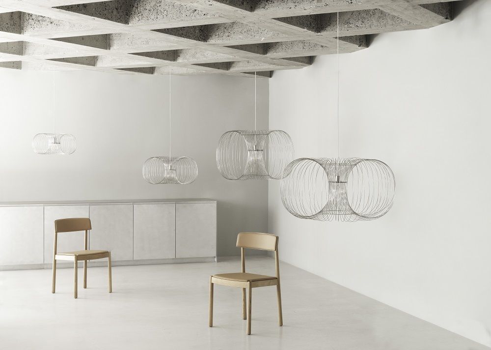 Coil Lampe von Normann Copenhagen: Draht-Pendelleuchte in modernem Wohnraum mit Stühlen.