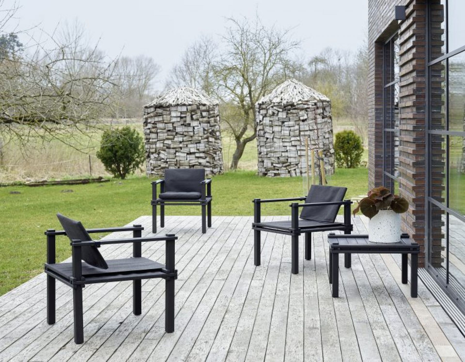 Drei schwarze Farmer Sessel Outdoor Cor und ein Beistelltisch auf einer Holzterrasse im Garten.