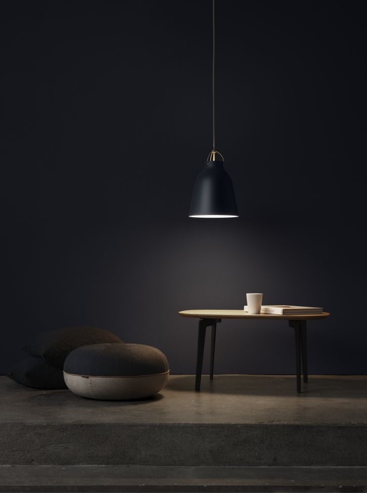 Schwarze Caravaggio Pendelleuchte von Fritz Hansen über kleinem Tisch mit Buch und Tasse in dunklem Raum.