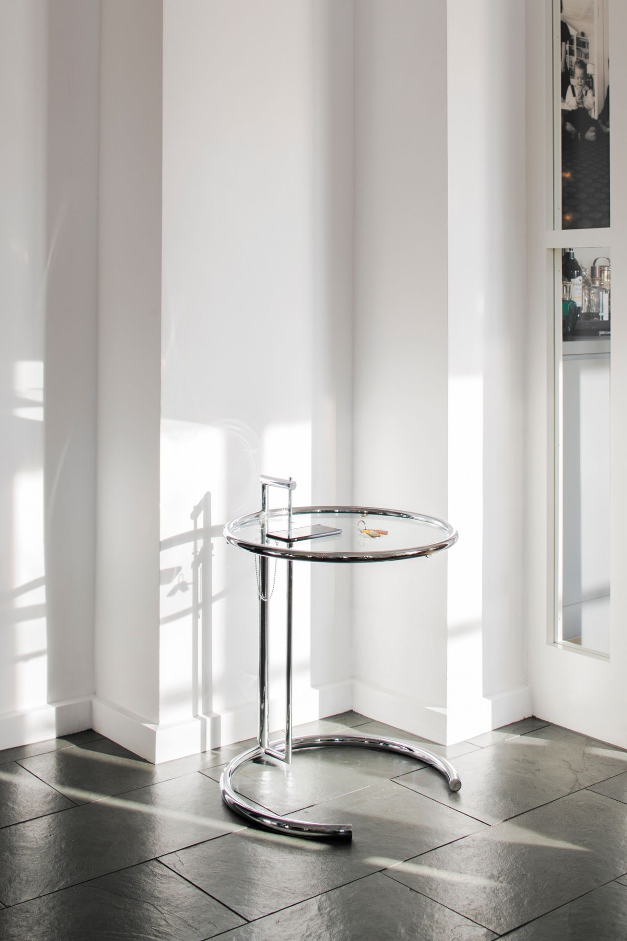 ClassiCon Adjustable Table E1027 Beistelltisch mit Glasplatte und verchromtem Stahlrohrgestell im hellen Raum.