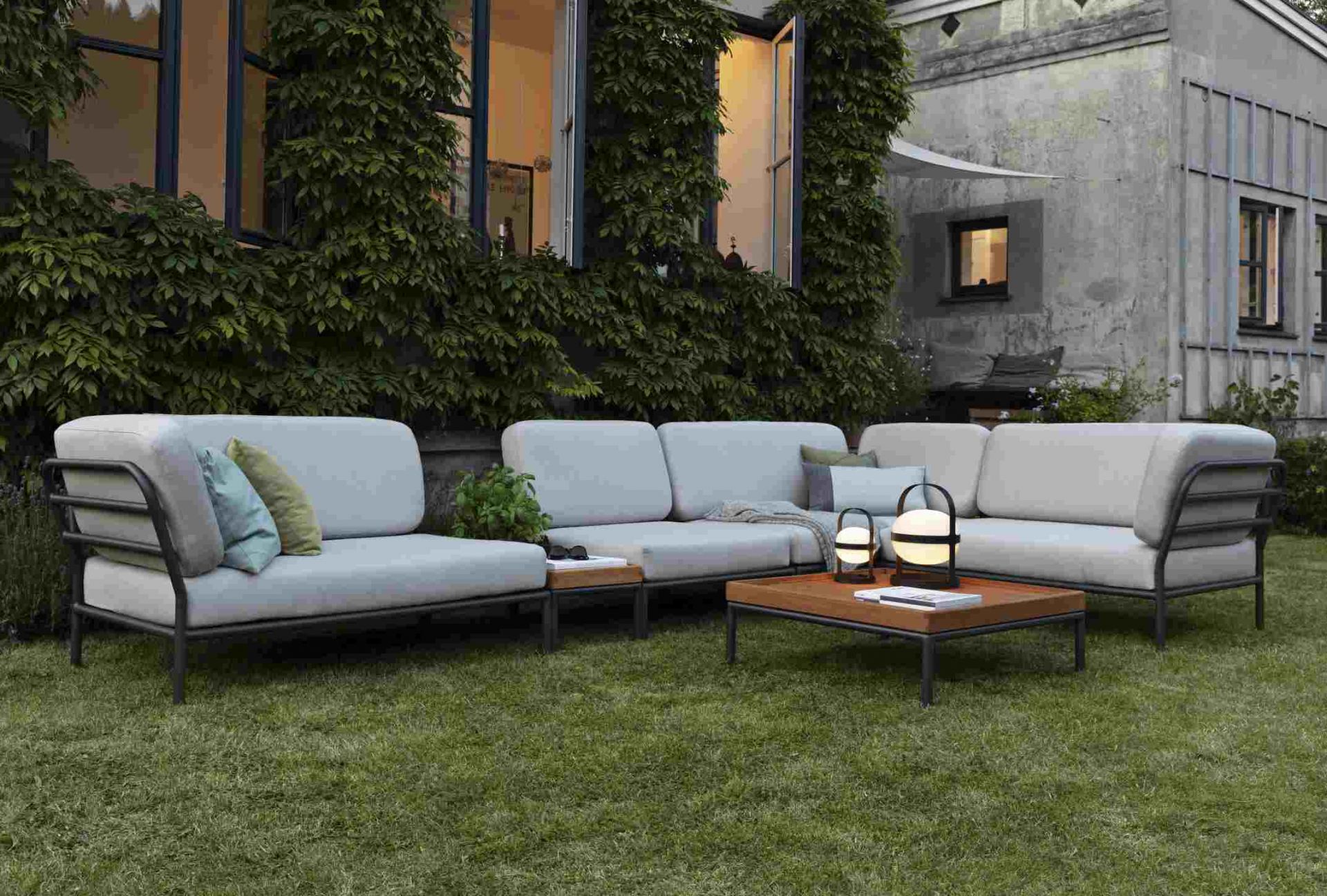 Houe Level Outdoor Lounge Sofa mit Couchtisch und Gartenbeleuchtung auf einer grünen Rasenfläche.