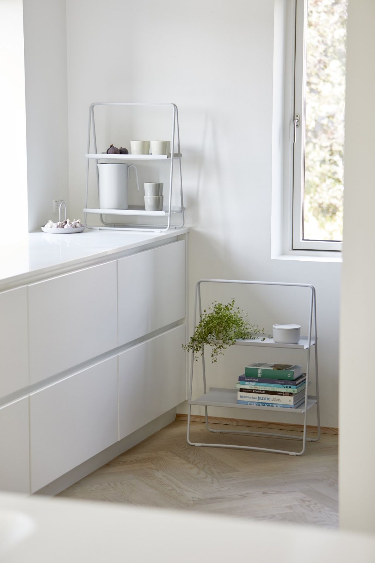 Helles Interieur mit zwei grauen A-Table Regalen von Zone Denmark, dekoriert mit Geschirr, Pflanzen und Büchern.
