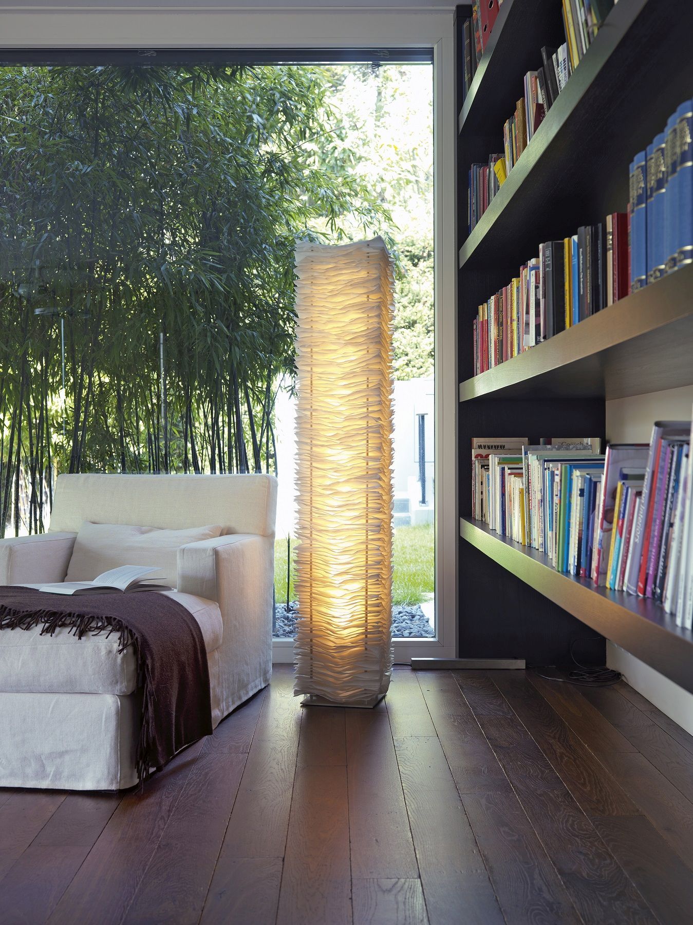 Moderne Stehlampe aus Papier in Wohnzimmer mit Sofa und Bücherregal, warmes Licht.