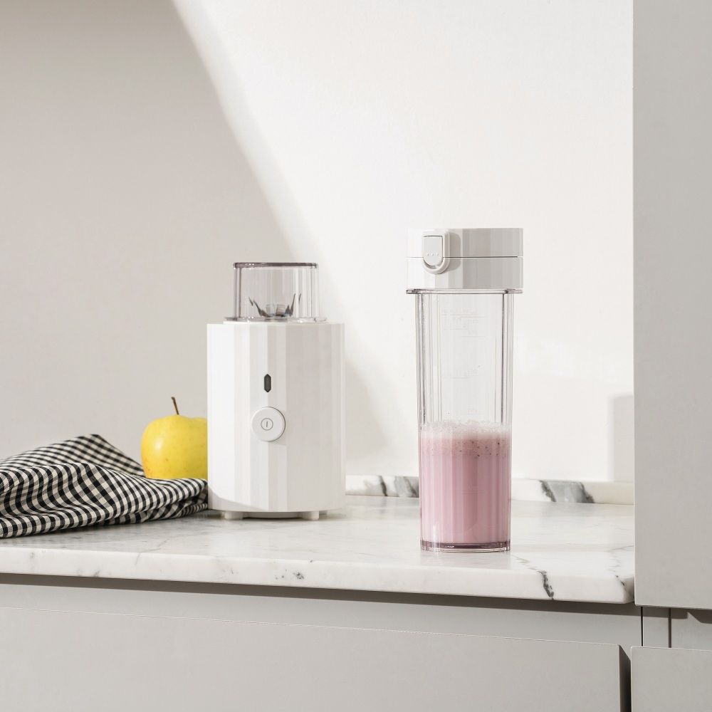 Weißer Plissé Smoothie Maker von Alessi neben rosa Smoothie und gelbem Apfel.