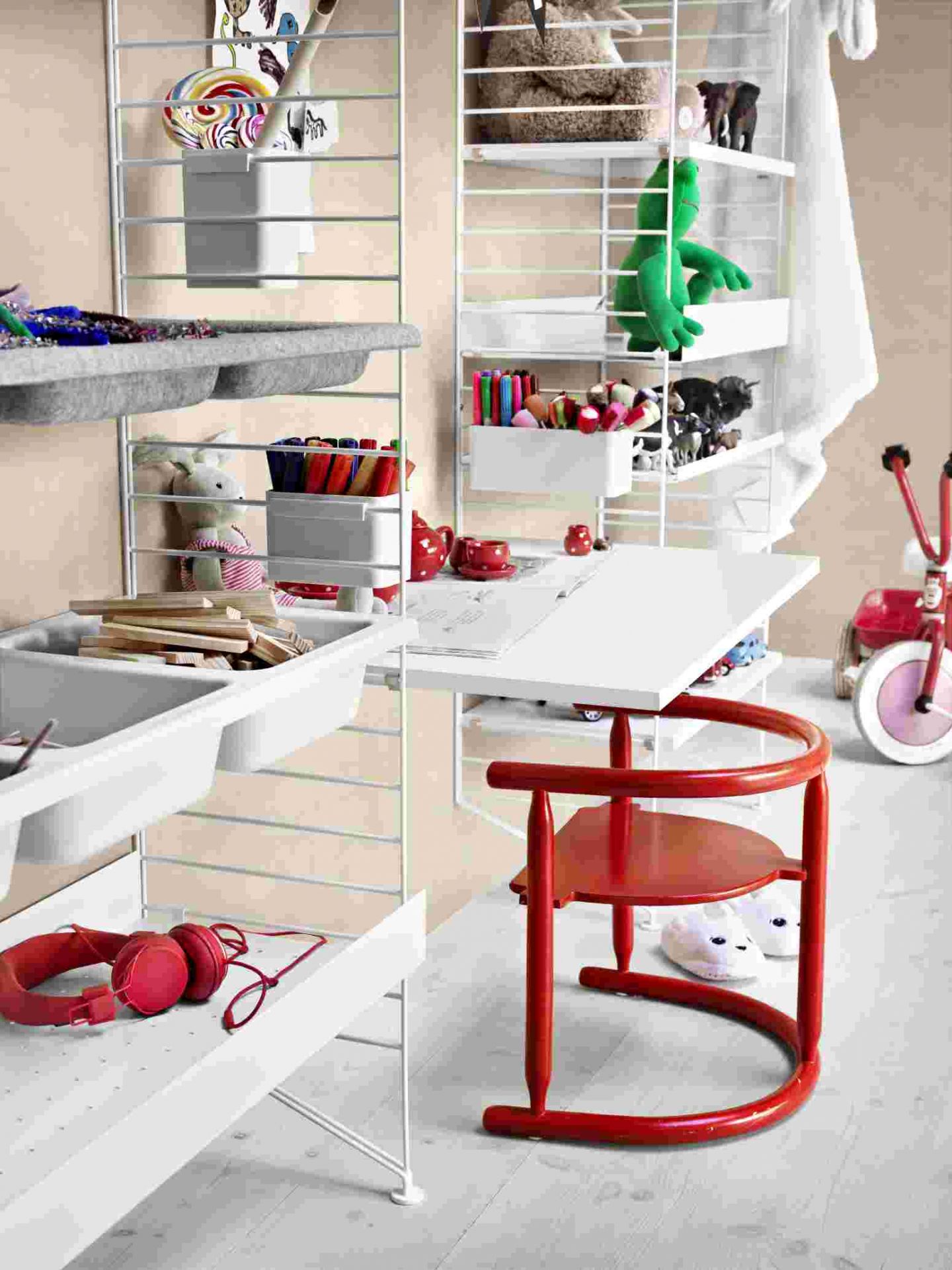 String Regal mit Arbeitsplatz: Weißes Regalsystem mit Schreibtisch und rotem Kinderstuhl im Kinderzimmer.