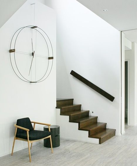 Delmori Clock Wanduhr von Nomon in modernem Interieur mit Treppe, Sessel und minimalistischem Design.
