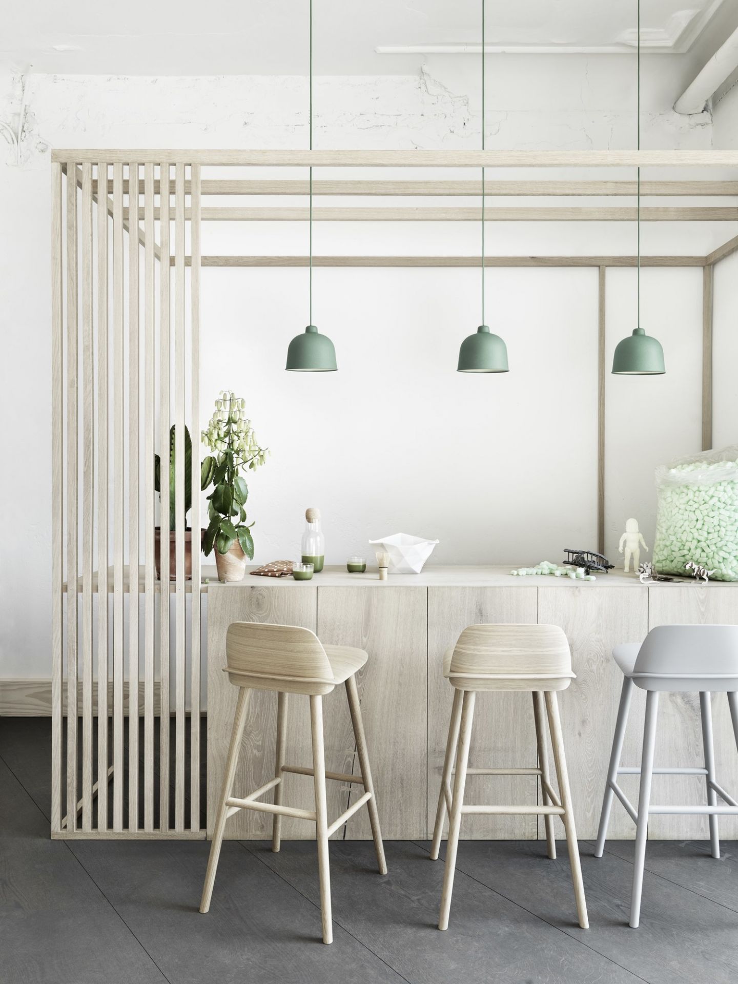 Drei grüne Muuto Grain Pendelleuchten über einer Küchentheke mit Holzhockern und dekorativen Elementen.