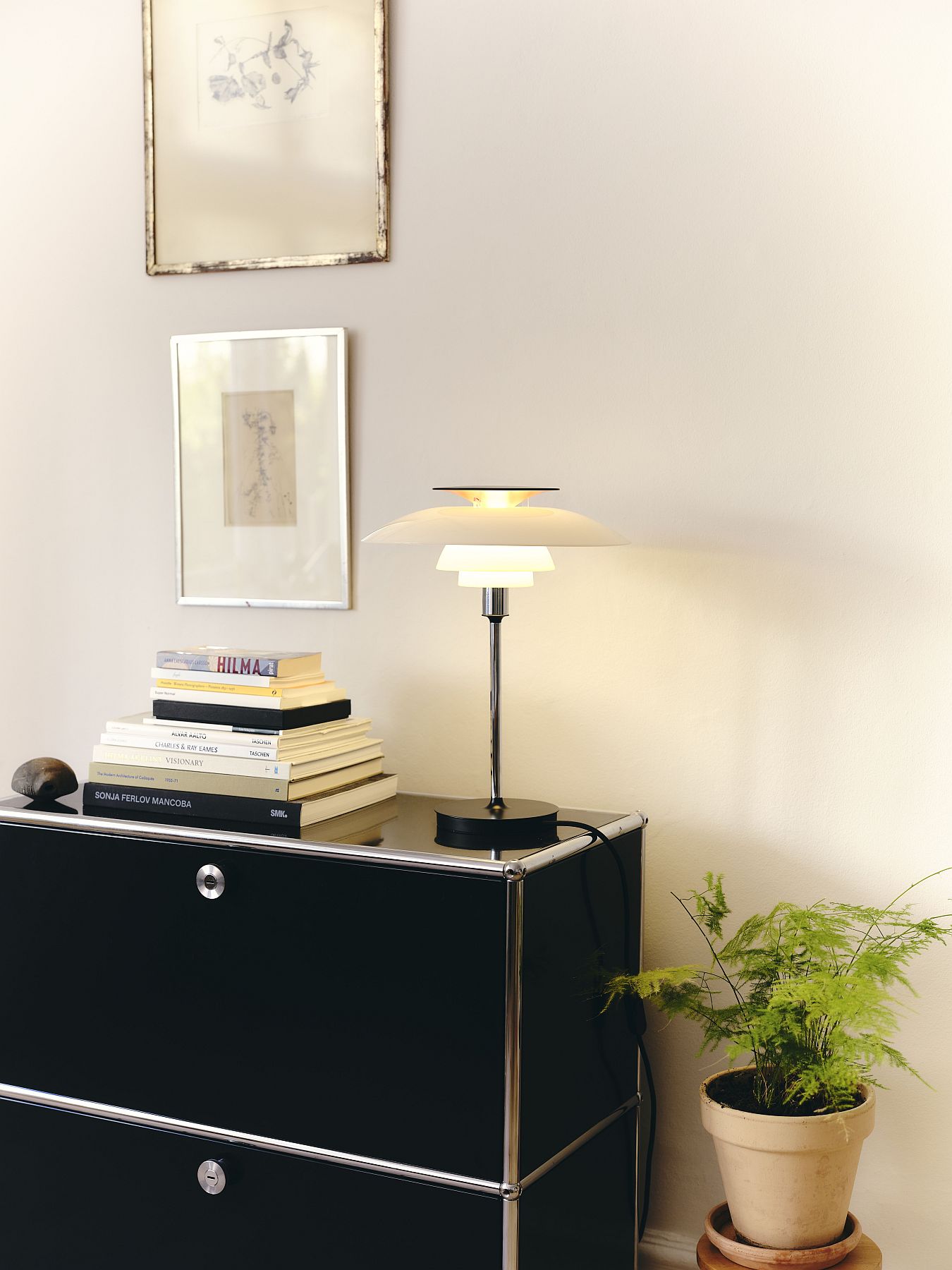 PH 80 Tischleuchte von Louis Poulsen auf schwarzem Sideboard mit Büchern und Zimmerpflanze.