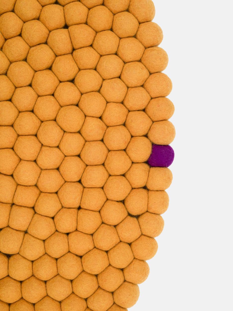 Detailaufnahme: Gelber Filzteppich "Big One" von myfelt (Ø 160 cm) mit einer einzelnen lila Filzkugel.