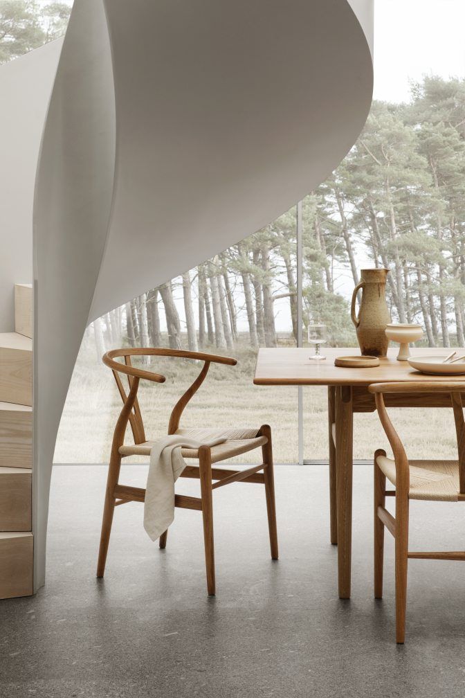 Essgruppe mit Teakholztisch und sechs CH24 Wishbone Stühlen von Carl Hansen & Søn vor Fenster.