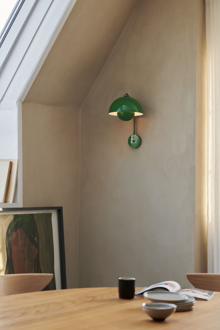 Grüne Flowerpot Wandleuchte von AndTradition an beiger Wand über Esstisch mit Geschirr und Dekoration.