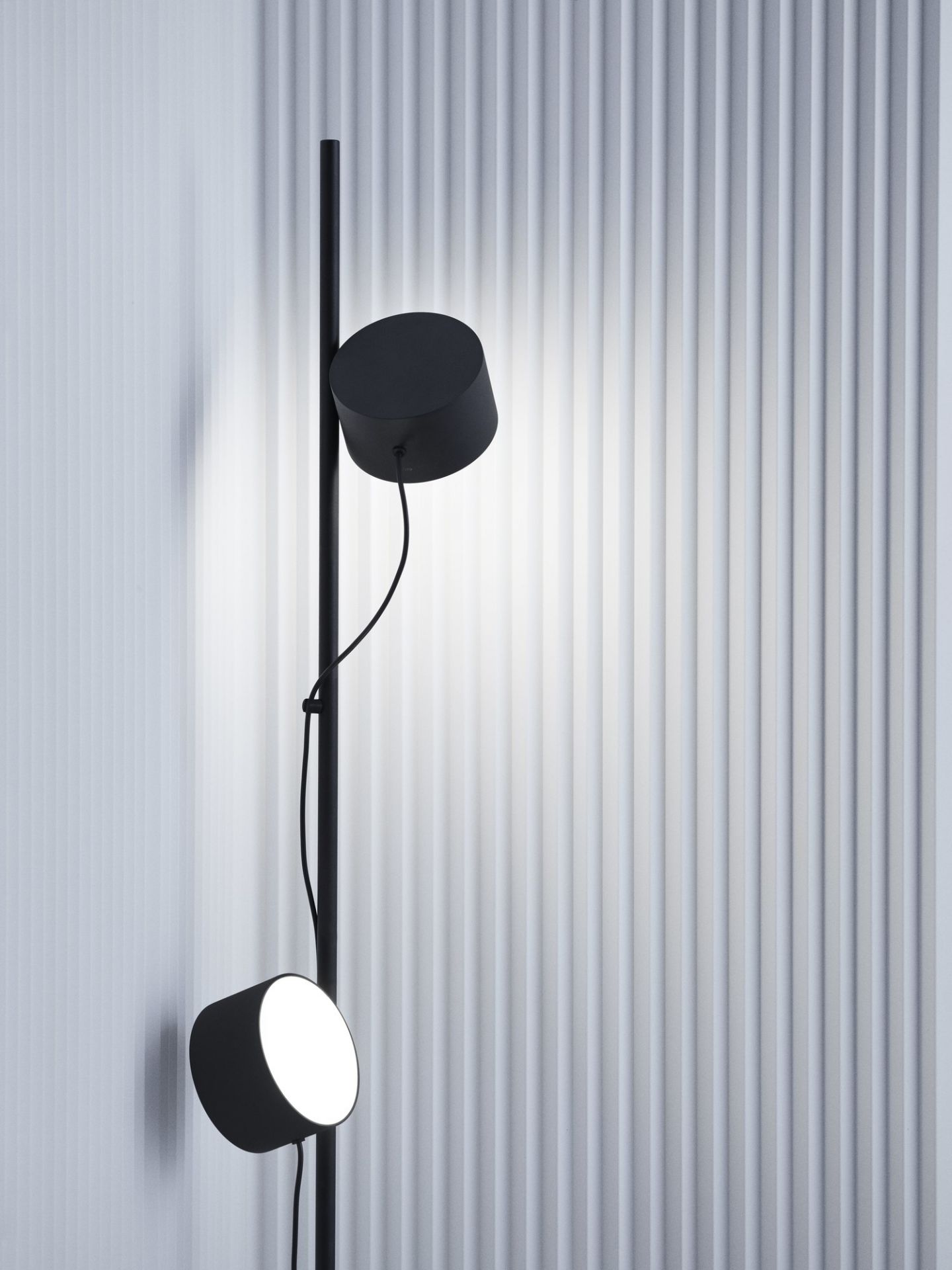 Schwarze Muuto Post Floor Lamp Stehleuchte mit zwei verstellbaren Leuchten vor einer Wand.