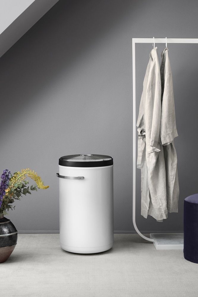 Weißer Vipp Wäschekorb im modernen Badezimmer, daneben Kleiderständer und Blumen in dunkler Vase.