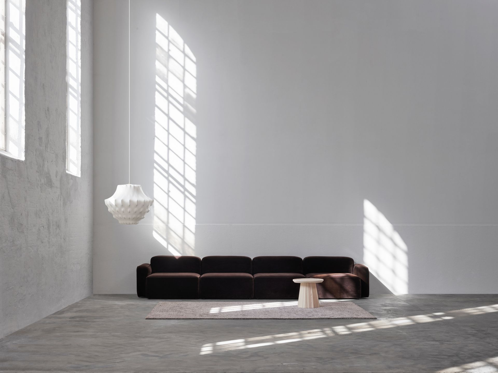 Weiße Phantom Lampe von Normann Copenhagen über braunem Sofa in minimalistischem Raum mit Tageslicht.