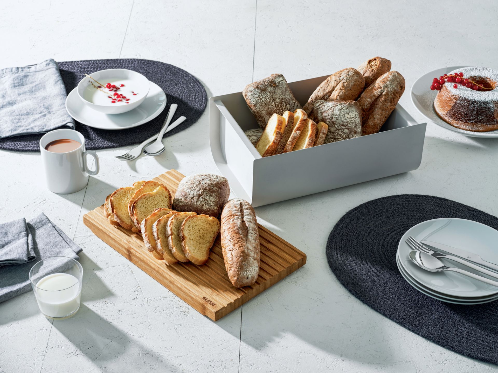 Alessi Mattina Brotkasten in warmem Grau mit Brot und Frühstücksgedecken auf einem Tisch.