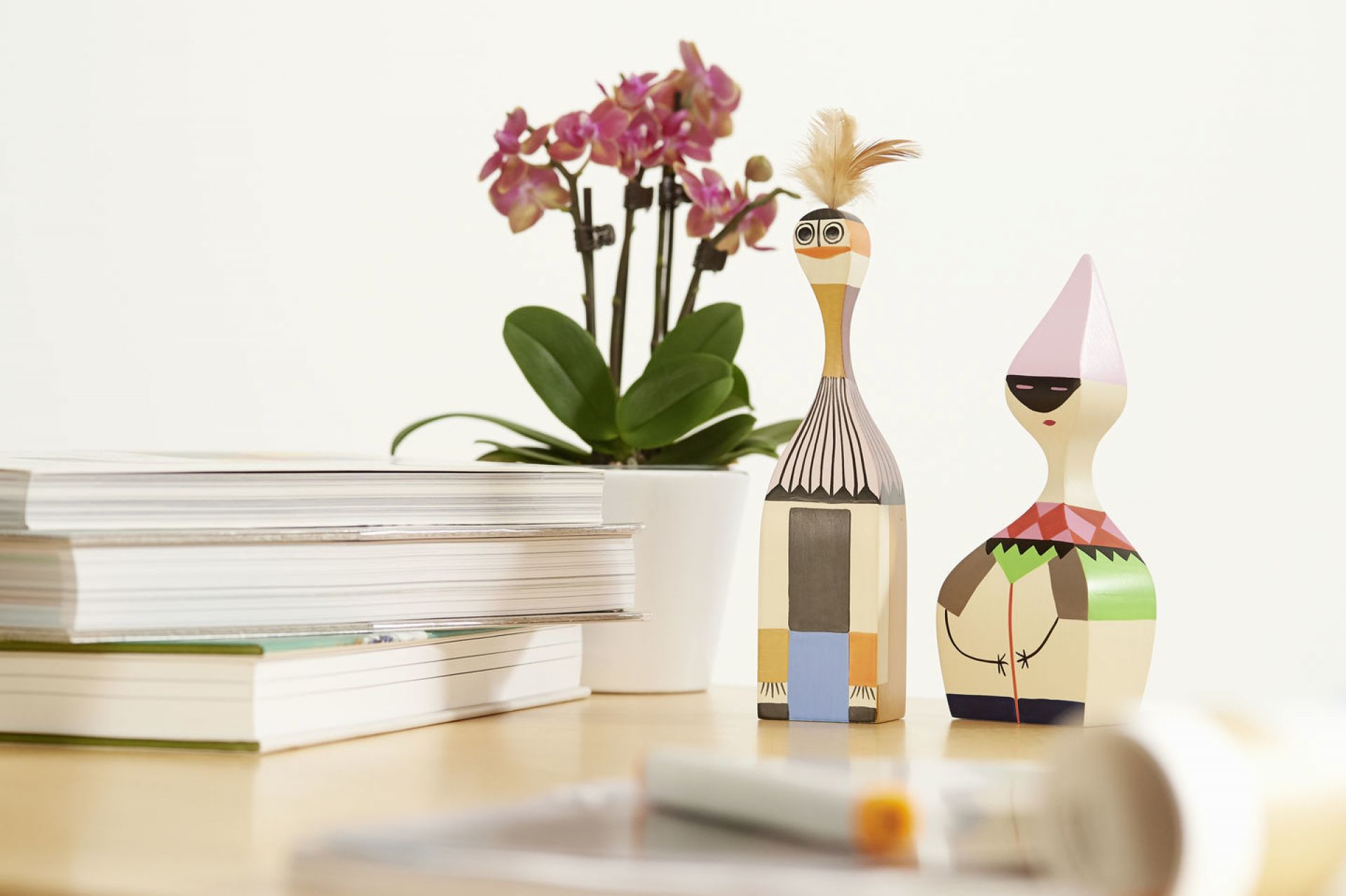 Nahaufnahme von zwei Wooden Dolls Holzfiguren von Vitra, mit Büchern und Orchidee.