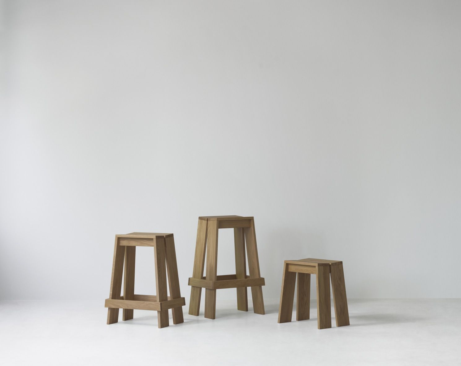 Drei hölzerne Barhocker, unterschiedliche Höhen, Modell Let Barstool von Normann Copenhagen, minimalistisches Design.