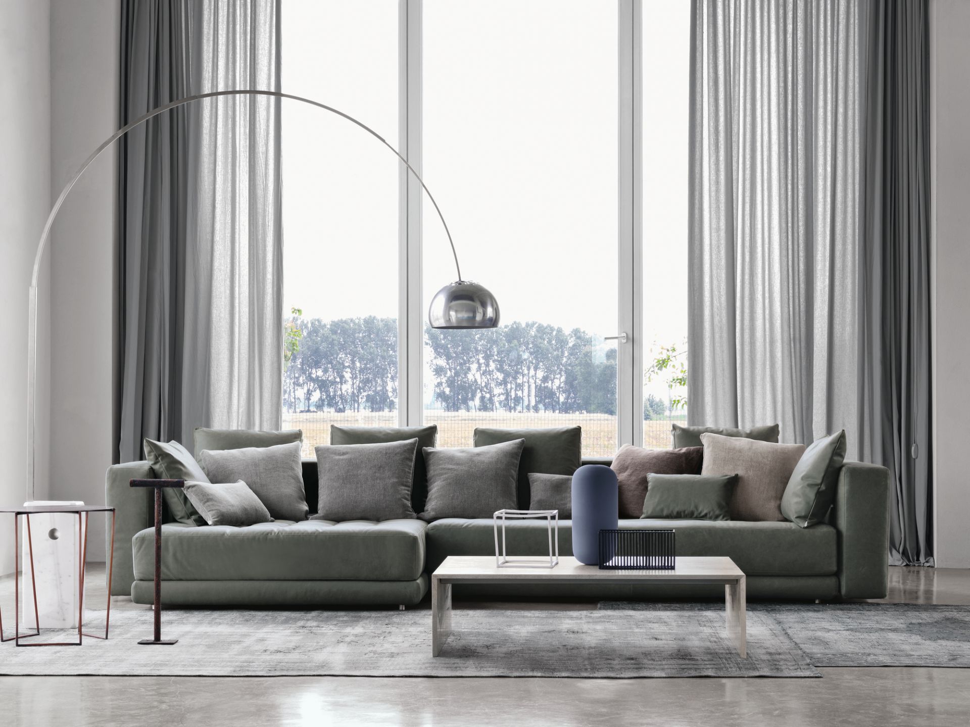 Arco LED Stehleuchte von Flos im Wohnzimmer mit großem Sofa und Fenster.
