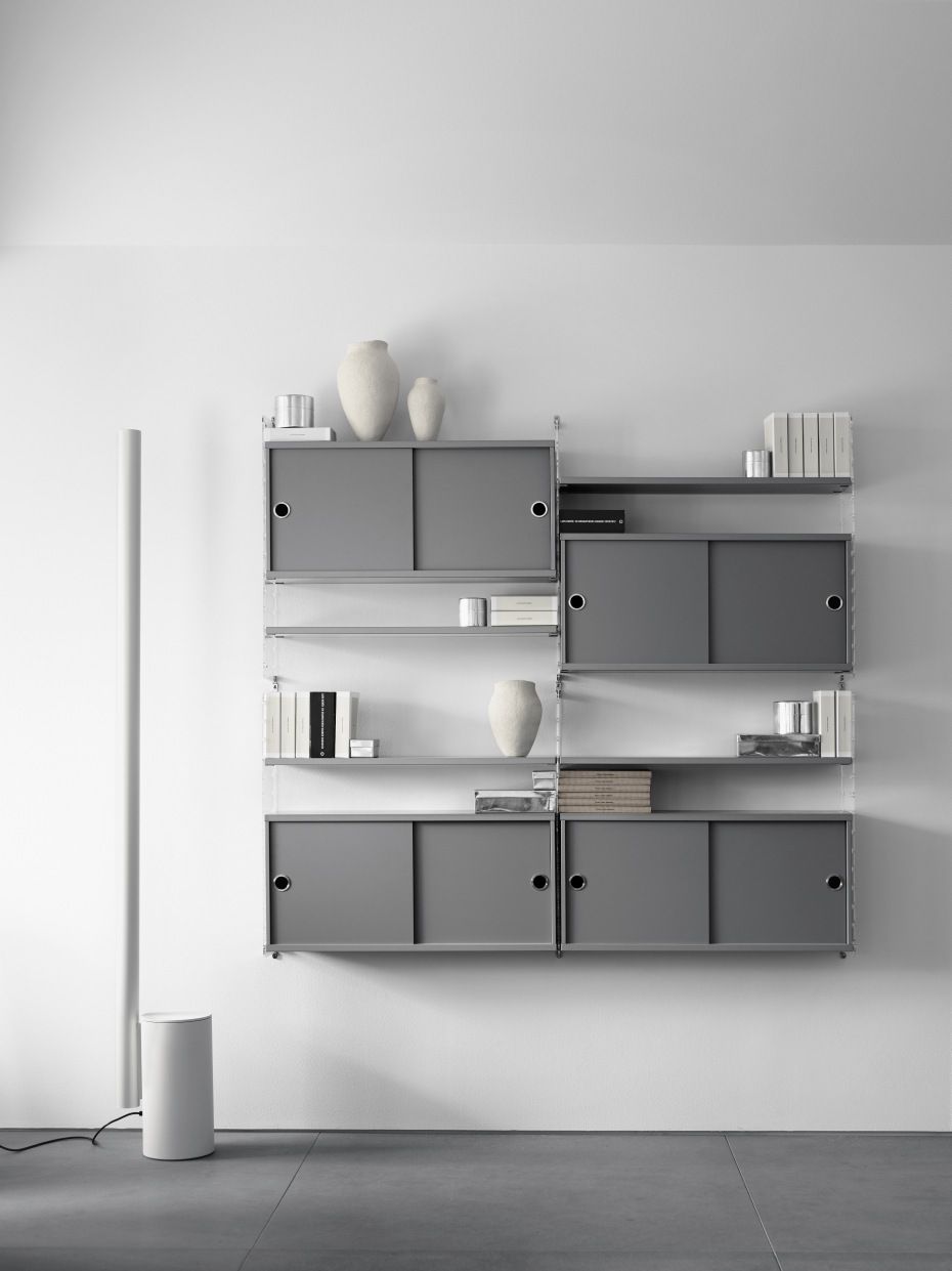 Graues String Regal-System "Wohnzimmer KONFIGURATIONEN L2" mit Schiebetüren und Dekorationsartikeln an weißer Wand.