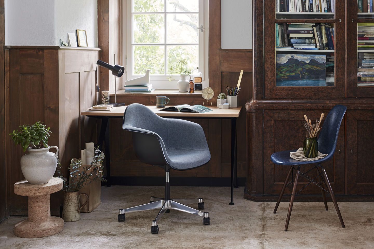 Vitra Eames Plastic Arm Chair DAL, vollgepolsterter Bürostuhl in Grau vor Schreibtisch und Fenster.