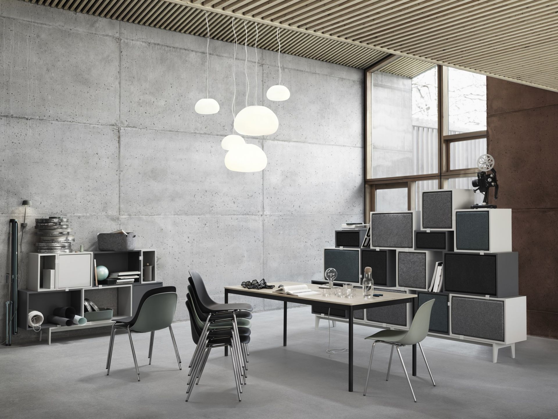 Moderne Büroeinrichtung mit Muuto Fluid Pendelleuchten, minimalistischem Tisch und Stühlen vor einer Betonwand.