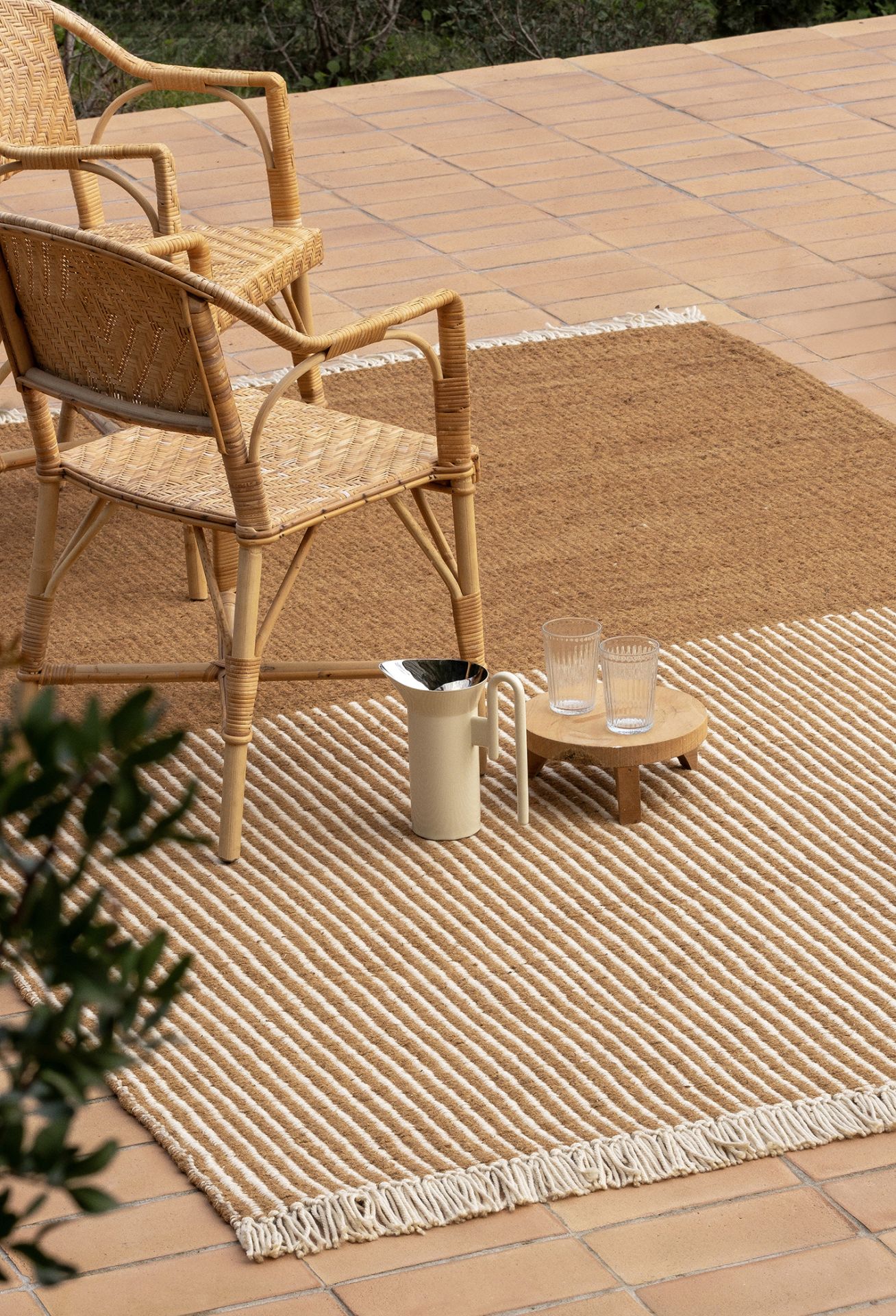 Nanimarquina Garden Outdoor Teppich mit Streifenmuster und Fransen auf einer Terrasse mit Stühlen.