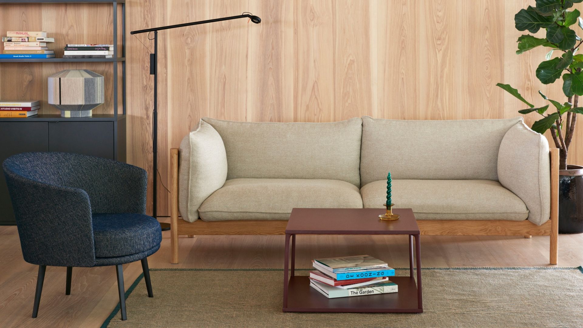 Wohnzimmer-Szene mit beigem Hay Sofa, blauem Sessel und gemustertem Tapis Teppich auf Holzboden.